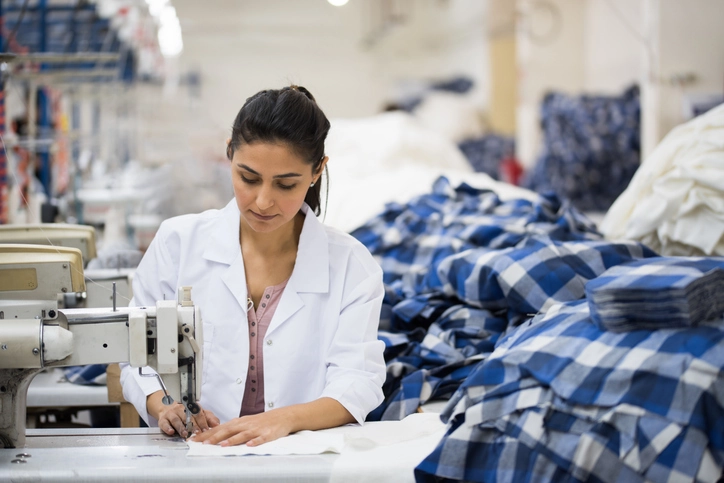 Positive young woman sewing with professional machine at workshop